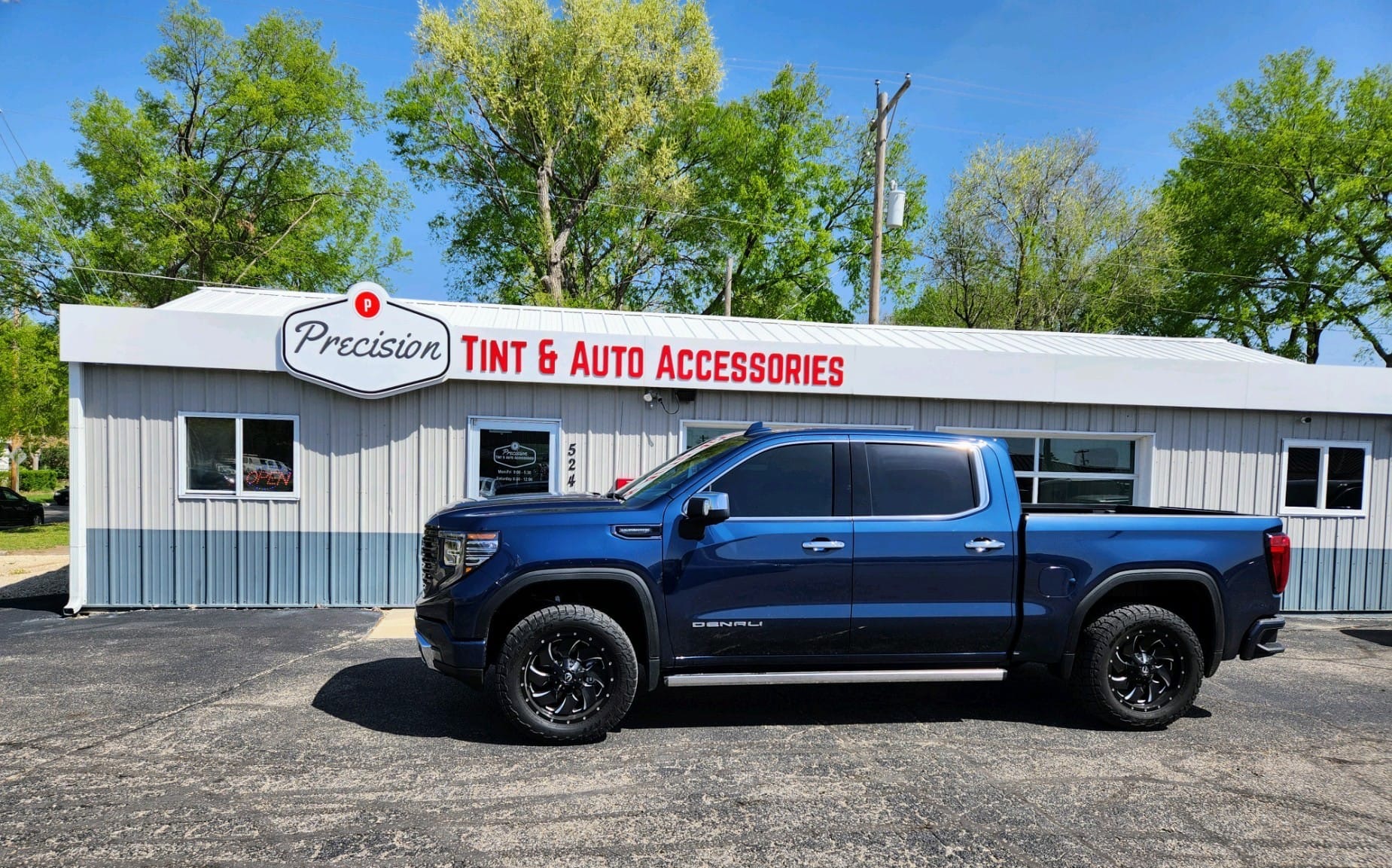 Blue GMC Sierra crew cab with dark tint in front of Precision Tint shop