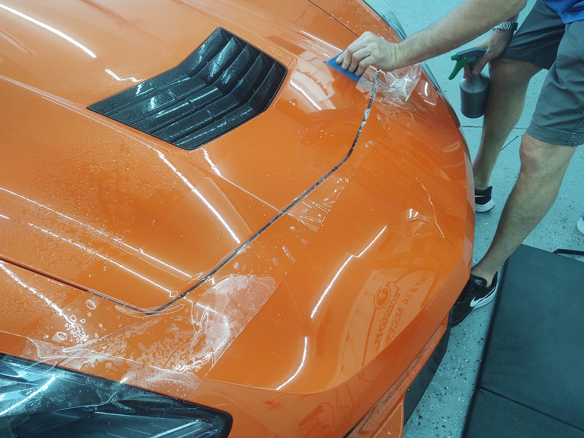 PPF being applied to orange Corvette rear deck, overhead action shot with squeegee