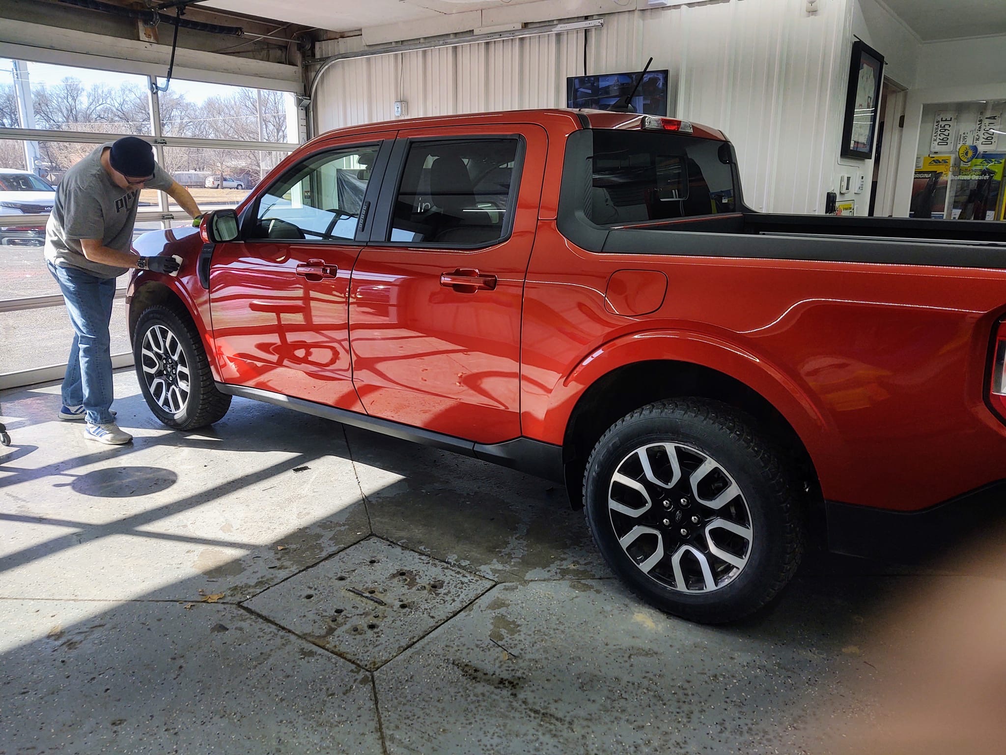 Red Ford Maverick in shop bay with installer working on tint