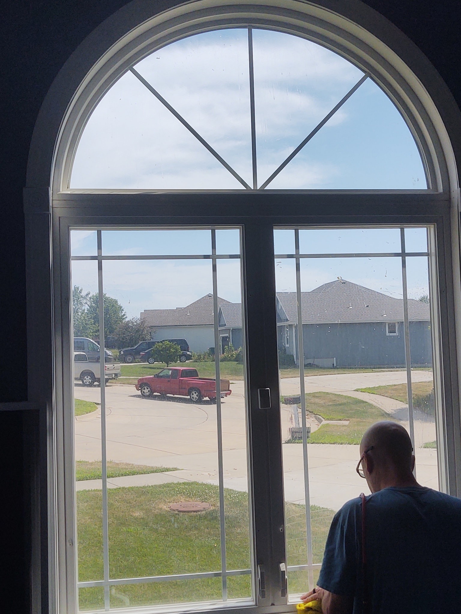 Installer applying tint to residential arched window, suburban view through glass