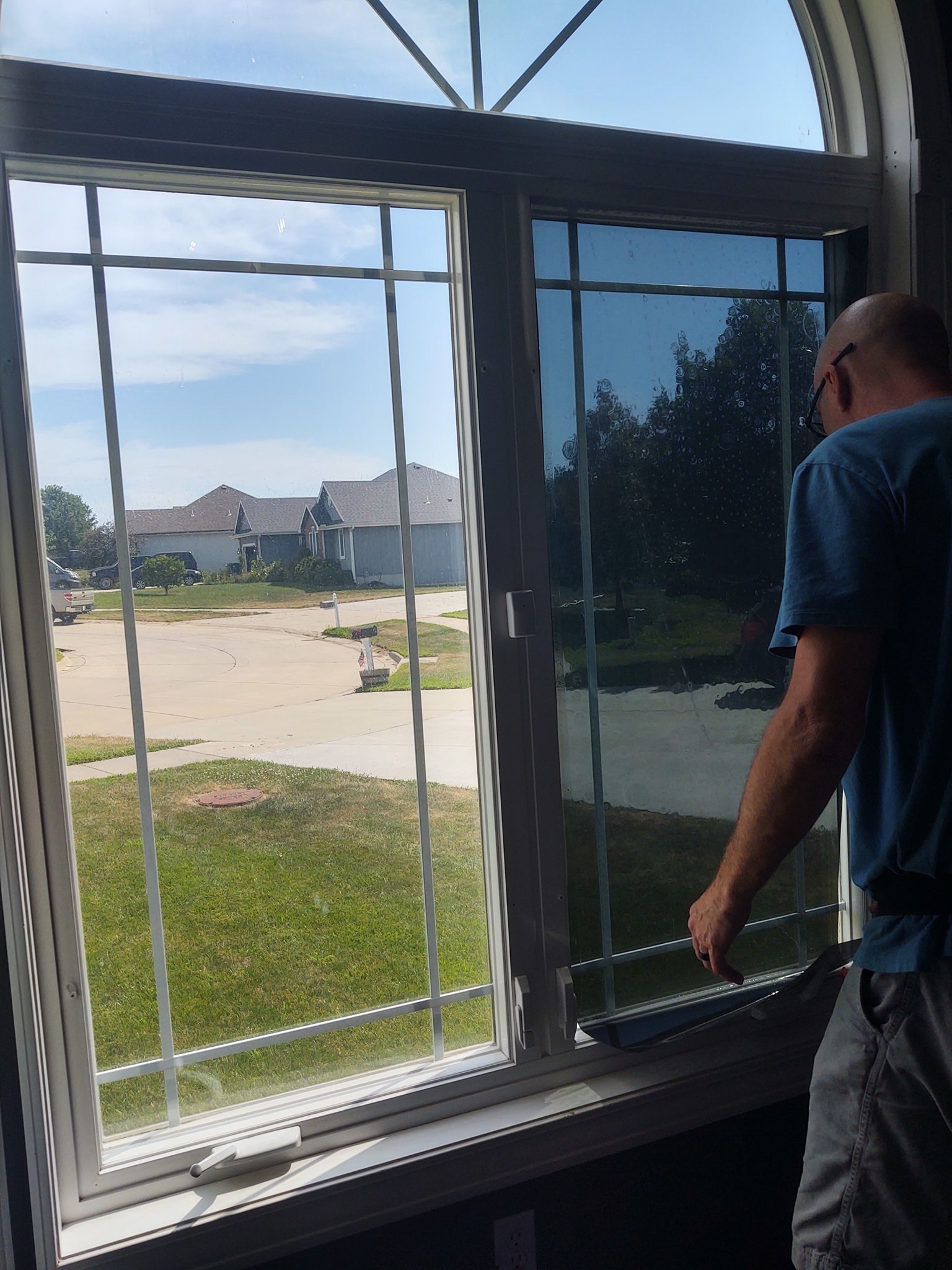 Installer applying tint to residential patio door, suburban neighborhood visible