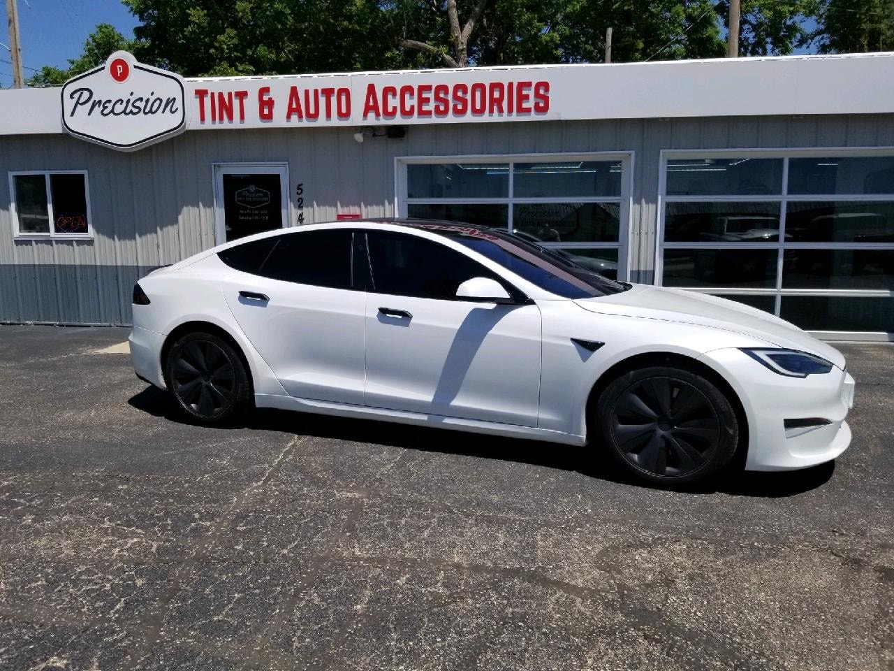 White Tesla Model S with dark ceramic tint, side profile in front of shop